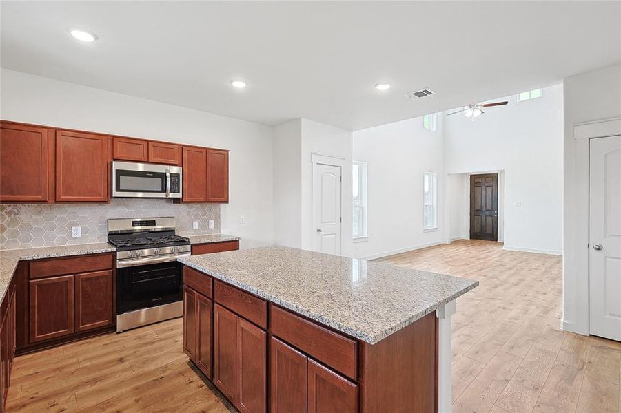 Kitchen featuring light wood-type flooring, decorative backsplash, appliances with stainless steel finishes, light stone countertops, and ceiling fan