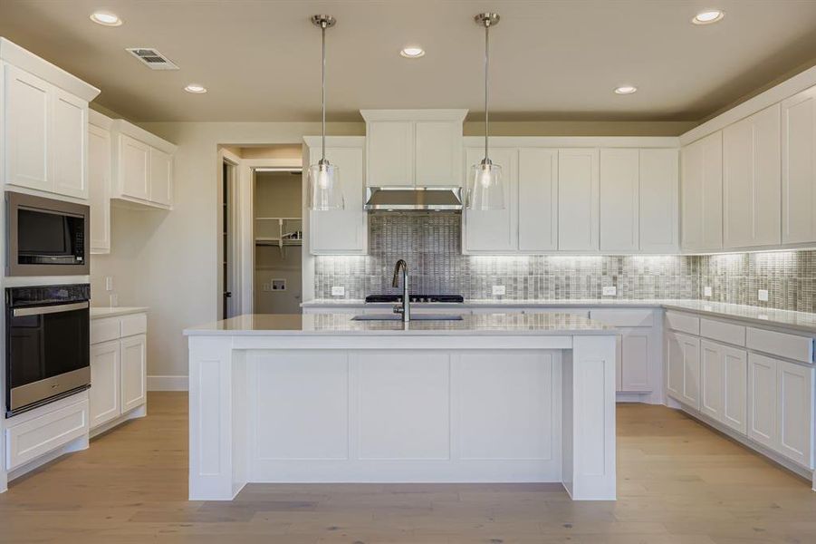 Kitchen with oven, a kitchen island with sink, white cabinets, recessed lighting, and light wood-style floors