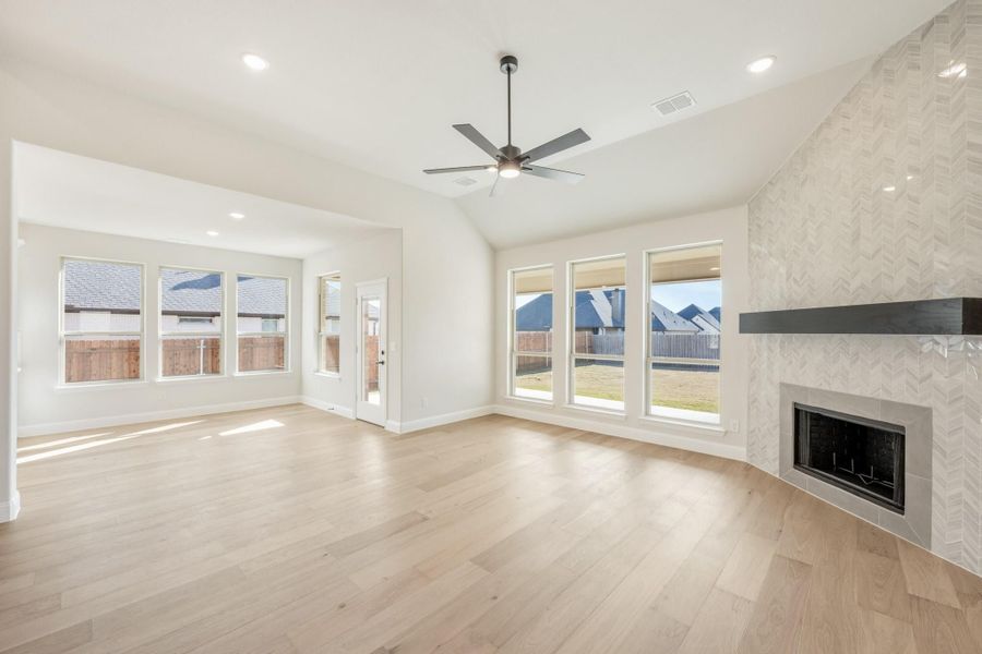 Open living room with light wood floors, tile fireplace, ceiling fan, and large windows