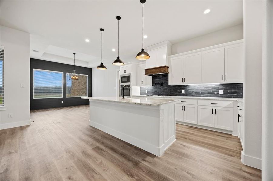 Kitchen with a center island with sink, white cabinetry, light stone countertops, hanging lights, and tasteful backsplash