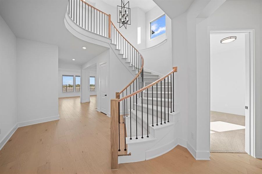 Staircase with plenty of natural light, wood finished floors, a high ceiling, a chandelier, and recessed lighting