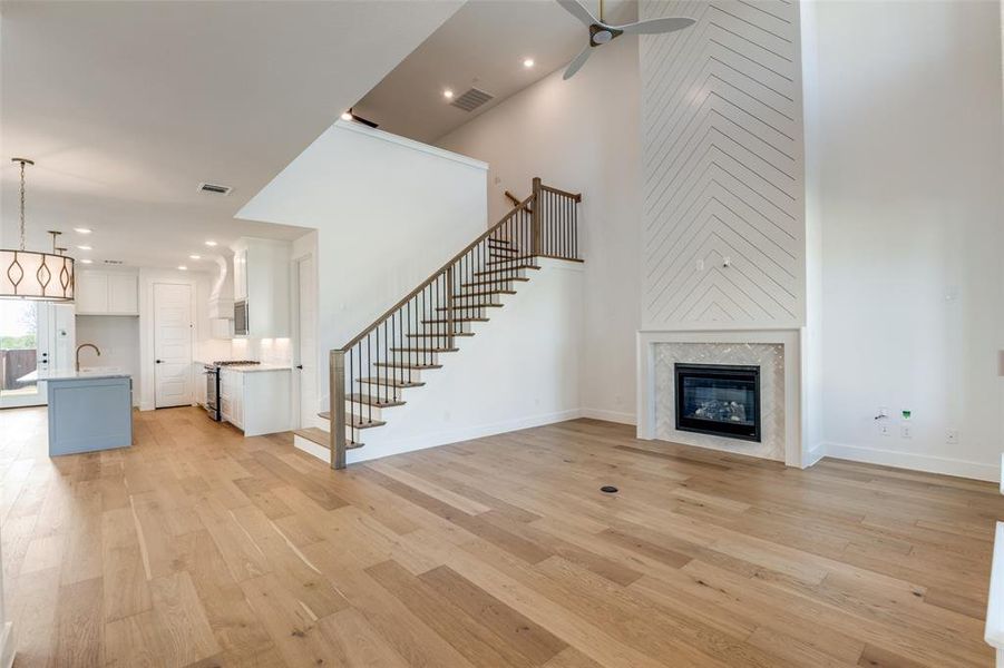 Unfurnished living room with sink, light hardwood / wood-style floors, a towering ceiling, ceiling fan, and a high end fireplace