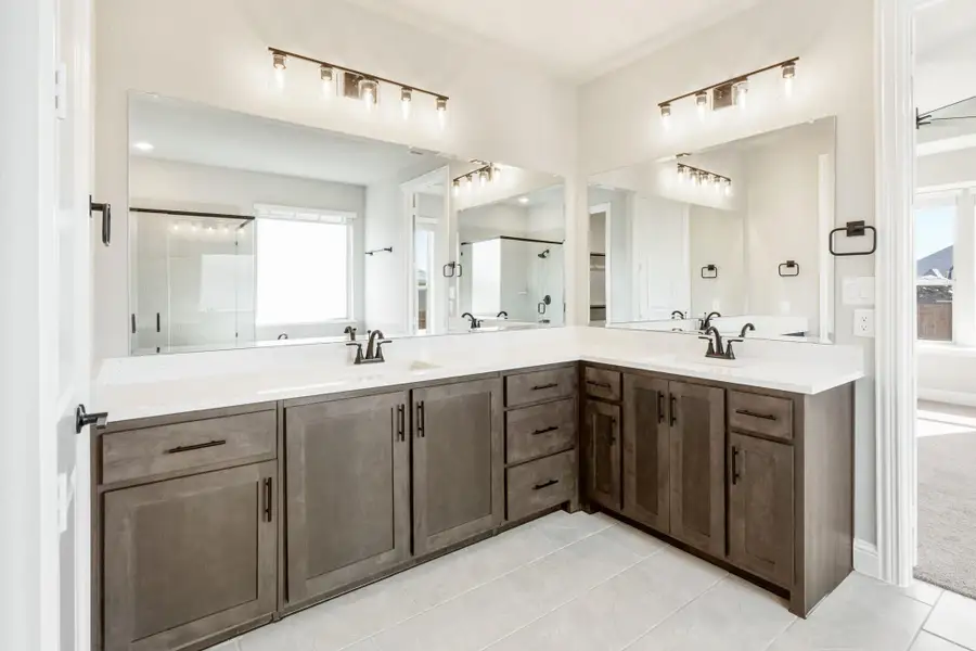 Master bathroom with dual sinks, dark wood L-shaped vanity, white countertops, and large mirrors with modern lighting