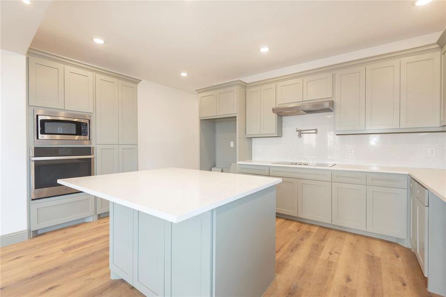 Kitchen with appliances with stainless steel finishes, recessed lighting, tasteful backsplash, light stone counters, and gray cabinetry