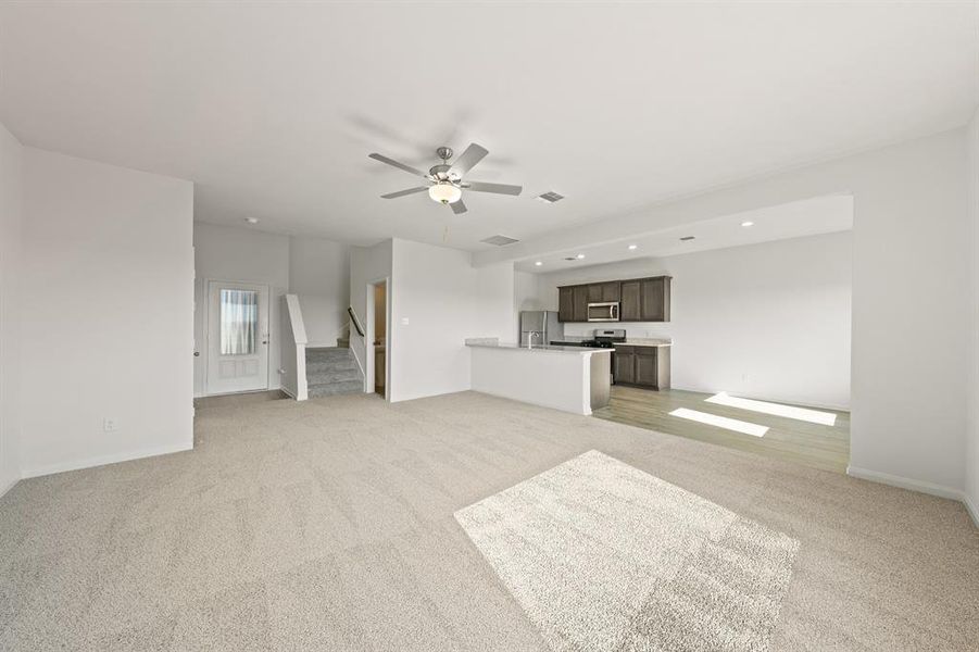 Unfurnished living room featuring light carpet, stairs, ceiling fan, and recessed lighting Unfurnished living room featuring light carpet, stairs, ceiling fan, and recessed lighting