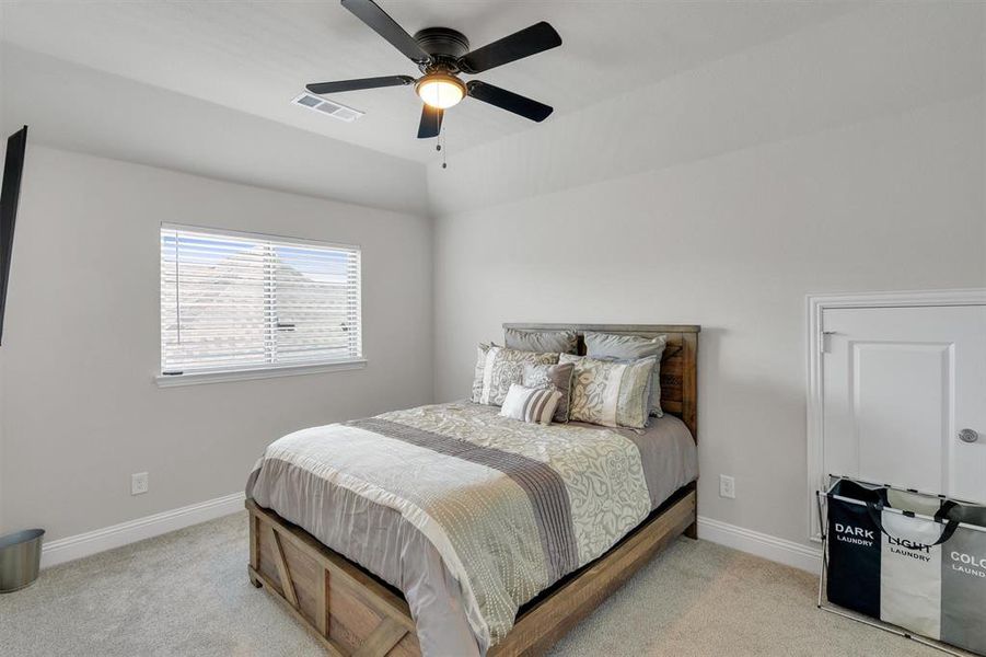 Bedroom featuring a wood-finish bed frame, light gray walls, plush carpet flooring, a window with horizontal blinds, and a ceiling fan with integrated lighting