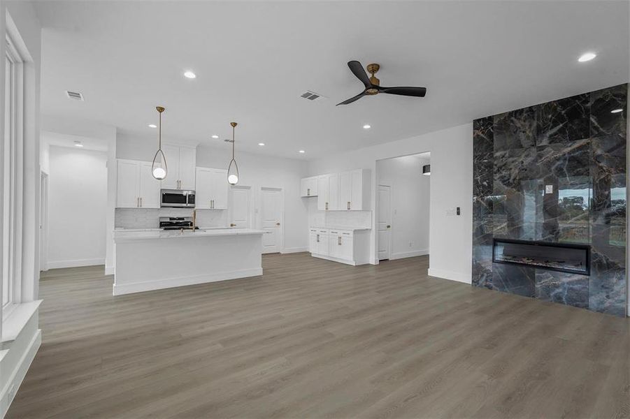Unfurnished living room with ceiling fan, light wood-type flooring, a high end fireplace, and recessed lighting Unfurnished living room with ceiling fan, light wood-type flooring, a high end fireplace, and recessed lighting