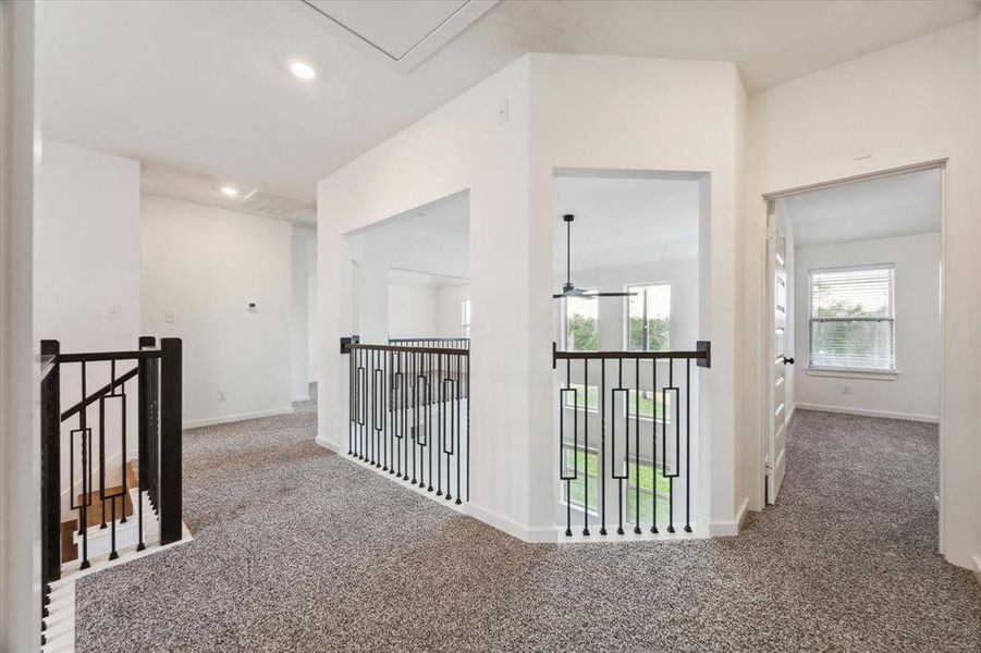 The upstairs hallway features a unique layout with open views to the living area below, creating a sense of connection throughout the home. The neutral carpeting and modern railing design add both comfort and style to this versatile space.