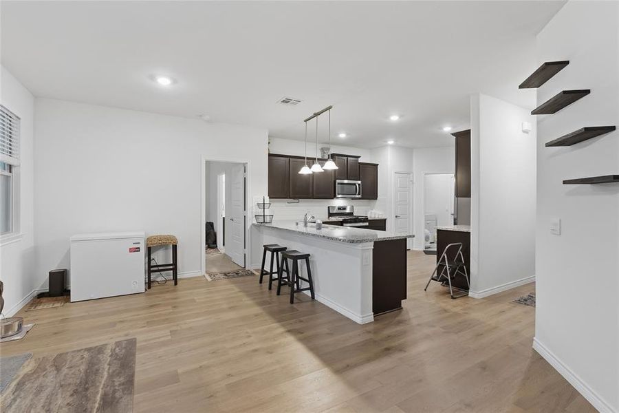 Open-concept kitchen and living area featuring wood-finish flooring, recessed lighting, and a kitchen island with seating