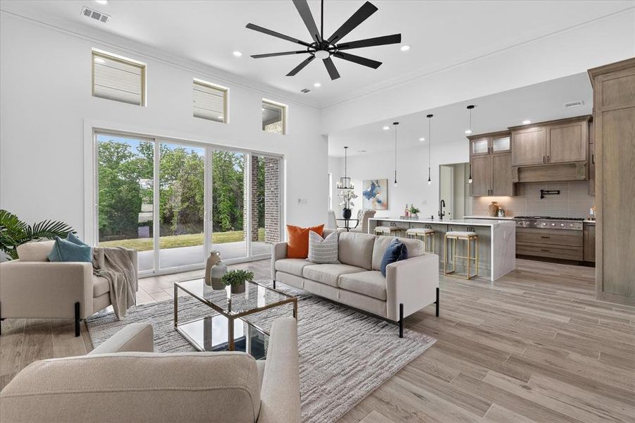 Living area featuring ceiling fan, light wood finished floors, a high ceiling, ornamental molding, and recessed lighting