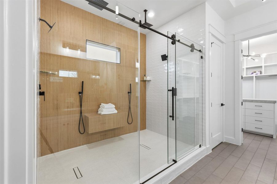 Step through the sliding glass door into an expansive walk-in shower featuring six showerheads and a serene design.