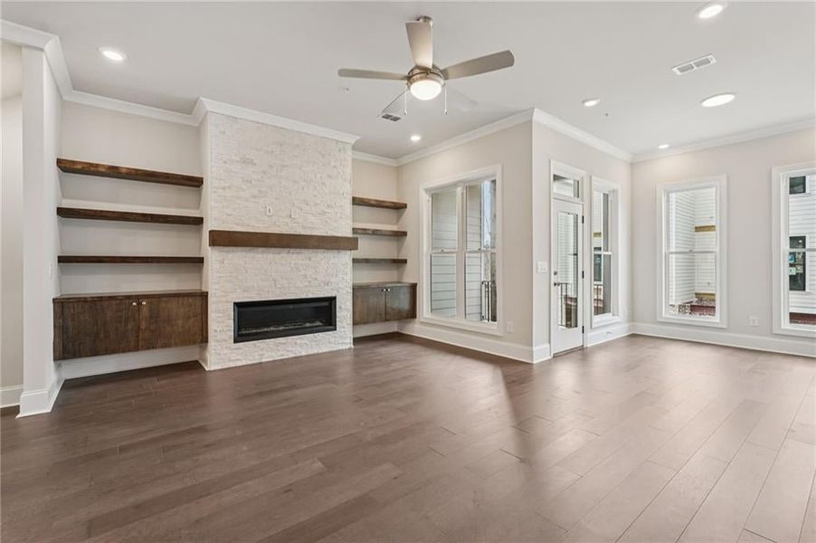 Unfurnished living room featuring ceiling fan, ornamental molding, a stone fireplace, recessed lighting, and dark wood-style flooring