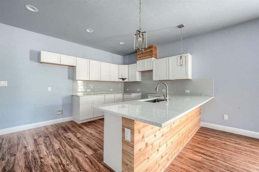 Kitchen featuring white cabinetry, sink, light hardwood / wood-style flooring, kitchen peninsula, and backsplash