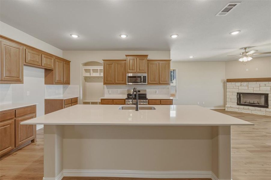 Kitchen island with an undermount sink, quartz countertop, wood-finish cabinetry, stainless steel appliances, and wood-finish flooring Kitchen island with an undermount sink, quartz countertop, wood-finish cabinetry, stainless steel appliances, and wood-finish flooring