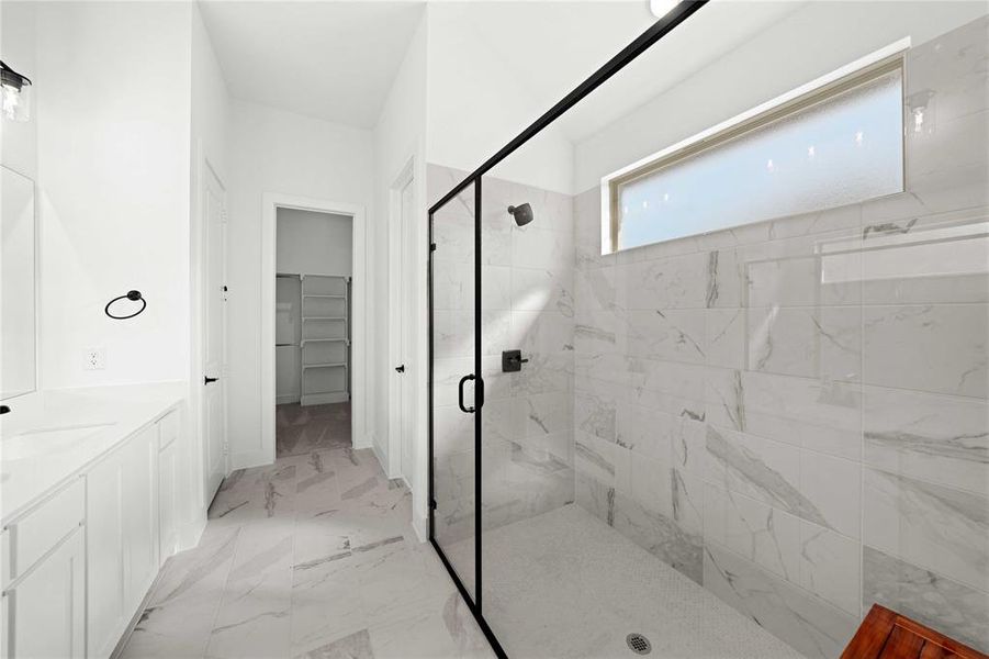 Full bathroom featuring a marble finish shower, a spacious closet, vanity, and light marble finish floors Full bathroom featuring a marble finish shower, a spacious closet, vanity, and light marble finish floors