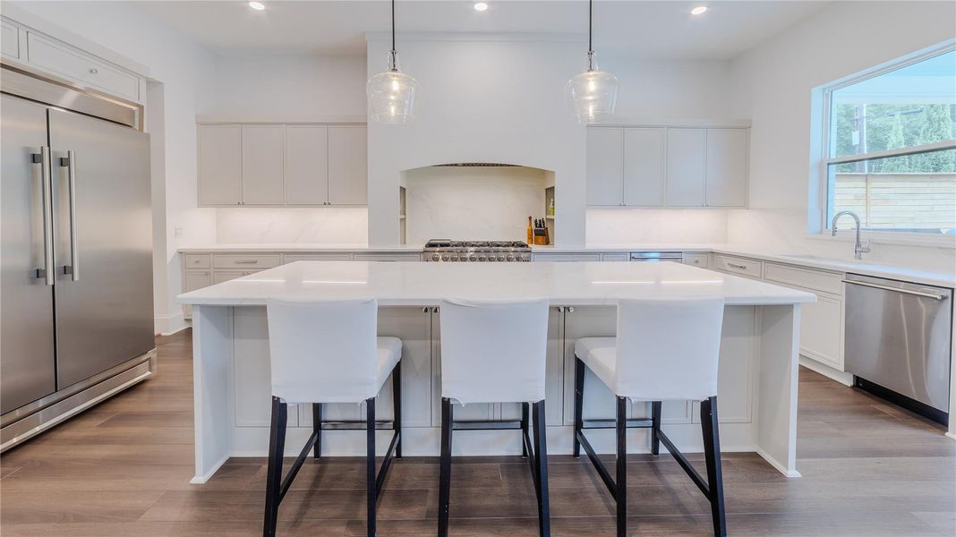 This modern kitchen features a spacious island with seating for three, sleek cabinetry, stainless steel appliances, and elegant pendant lighting, creating a bright and inviting space.