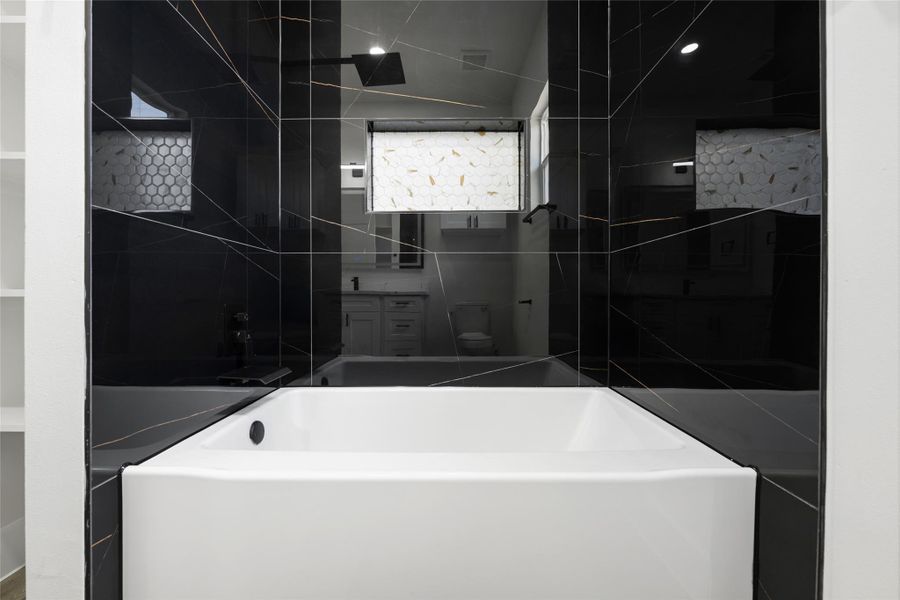 Corner soaking tub surrounded by black marble-look tile with white veining