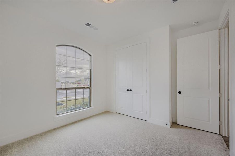 Room featuring light-colored carpeting, an arched window, white walls, and a pair of white bifold doors