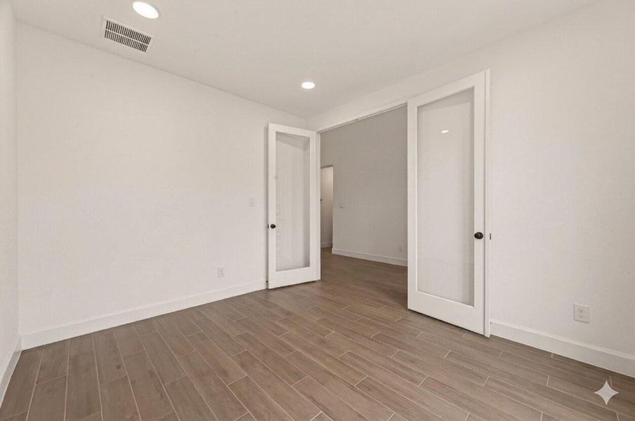 This photo shows a bright, empty room with light wood flooring and white walls. It features recessed lighting and French doors, creating an open and airy feel.