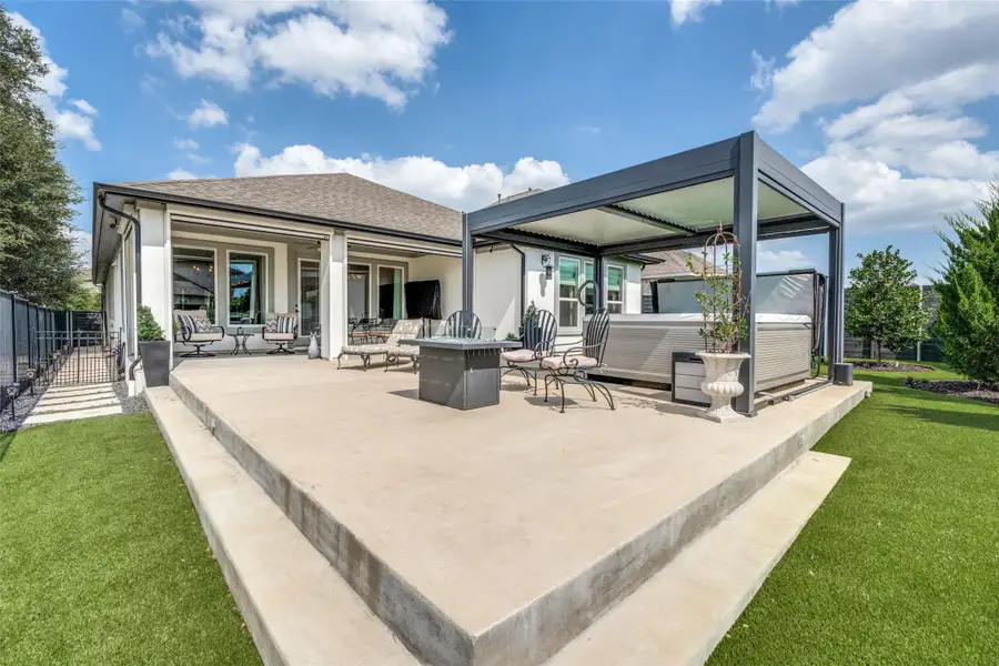 An expansive concrete patio extends from the home to a modern louvered pergola structure.