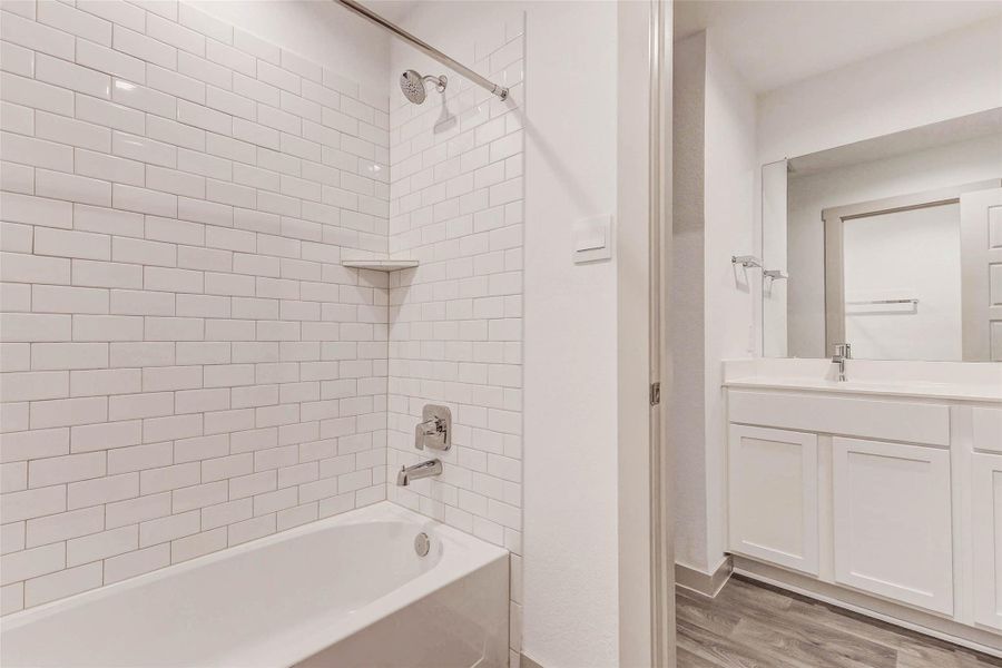 Clean, crisp, and classic, this secondary bath features a deep soaking tub with white subway tile surround and a built-in corner shelf. The view into the spacious vanity area showcases ample storage, a wide mirror, and wood-look flooring, offering both style and functionality. Clean, crisp, and classic, this secondary bath features a deep soaking tub with white subway tile surround and a built-in corner shelf. The view into the spacious vanity area showcases ample storage, a wide mirror, and wood-look flooring, offering both style and functionality.