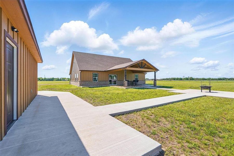 View of front of property with board and batten siding, a front lawn, covered porch, a shingled roof, and a rural view View of front of property with board and batten siding, a front lawn, covered porch, a shingled roof, and a rural view