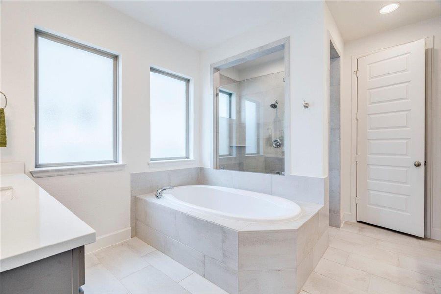The bathroom features an oval bathtub set into a tiled surround, a glass-enclosed shower, and a vanity with a light-colored countertop