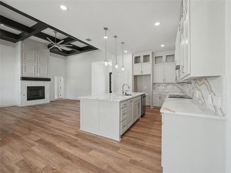 Open-concept living space with wood-finish flooring, a contemporary fireplace with a decorative mantel, and a coffered ceiling with a ceiling fan