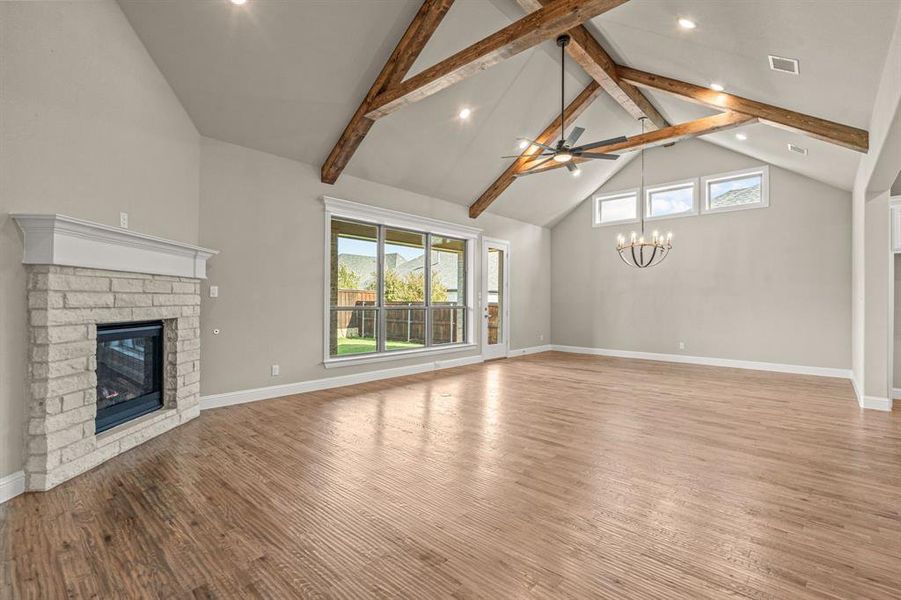 Unfurnished living room with high vaulted ceiling, a fireplace, beamed ceiling, wood finished floors, and a chandelier