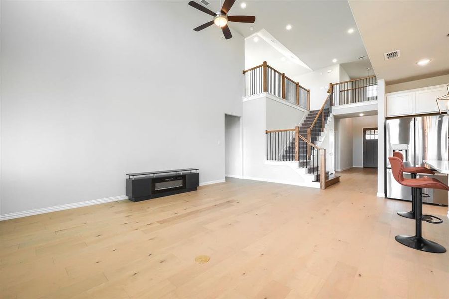 Living room featuring light wood-style flooring, a towering ceiling, recessed lighting, stairway, and a ceiling fan Living room featuring light wood-style flooring, a towering ceiling, recessed lighting, stairway, and a ceiling fan