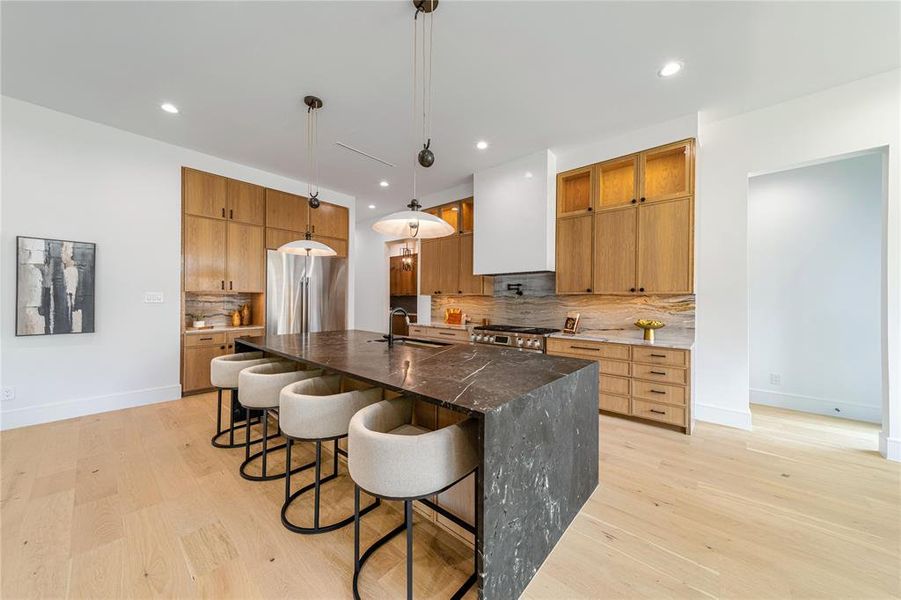 Kitchen featuring dark stone counters, light wood finished floors, hanging light fixtures, and a breakfast bar