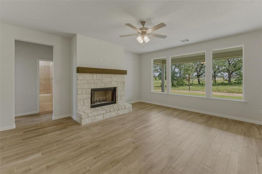 Spacious living area featuring wood-finish flooring, a stone fireplace with a wood mantel, and a ceiling fan