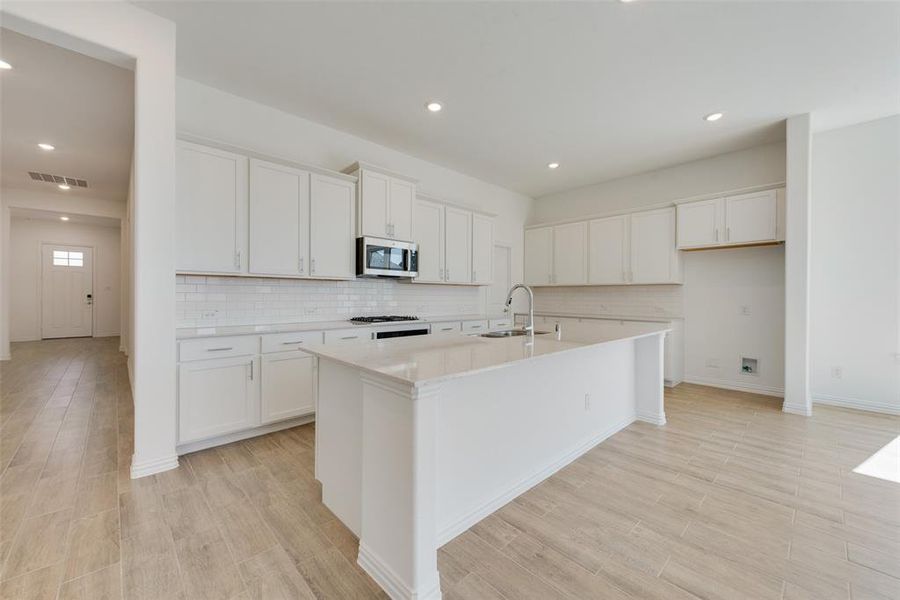 Kitchen featuring white cabinets, tasteful backsplash, sink, and a center island with sink