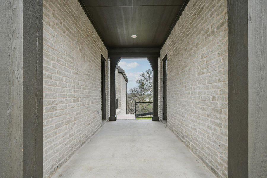 Exterior hallway featuring light-colored brick walls, a dark-stained wood ceiling, and concrete flooring Exterior hallway featuring light-colored brick walls, a dark-stained wood ceiling, and concrete flooring