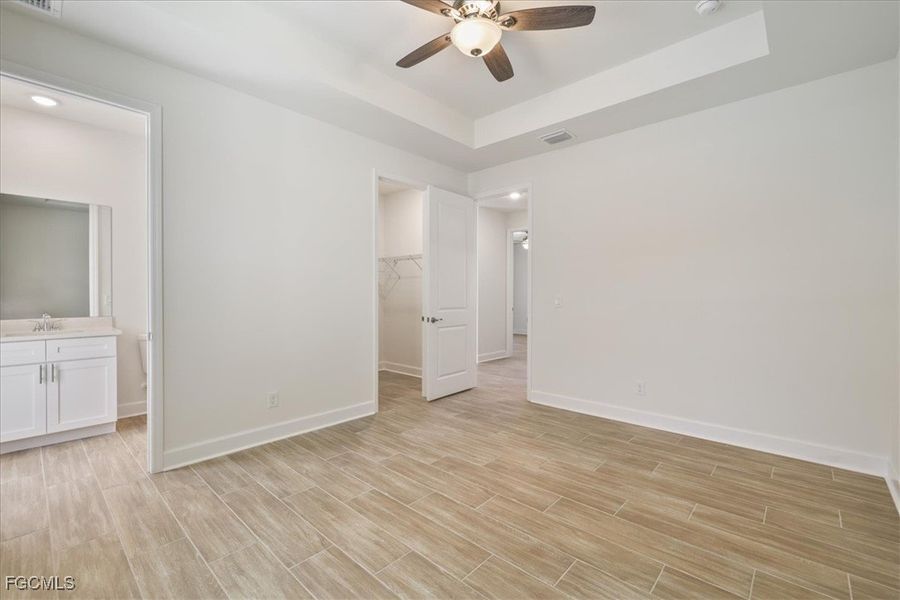 Unfurnished bedroom with connected bathroom, a spacious closet, wood finish floors, and a raised ceiling