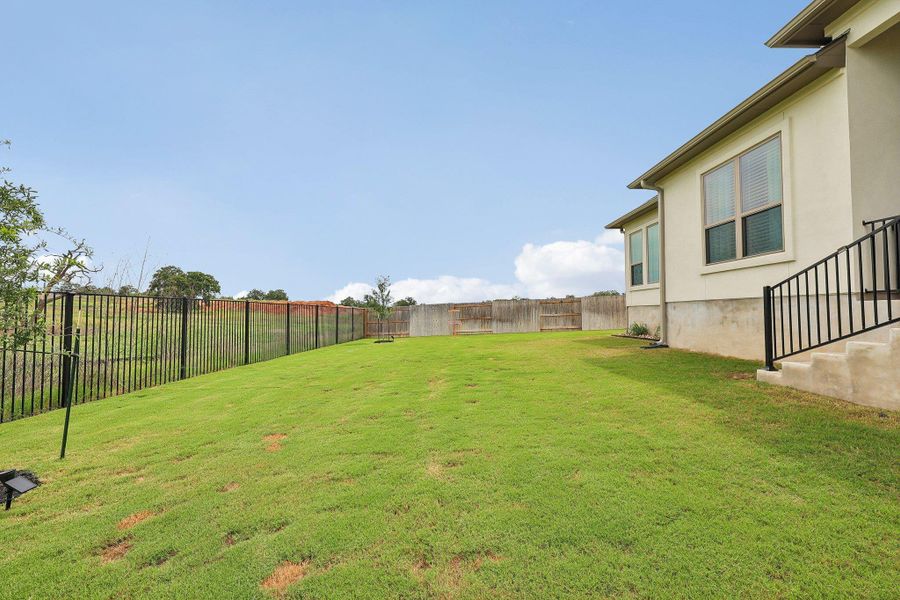Expansive backyard featuring a sloped lawn, black metal fencing, and a stucco exterior with multiple windows