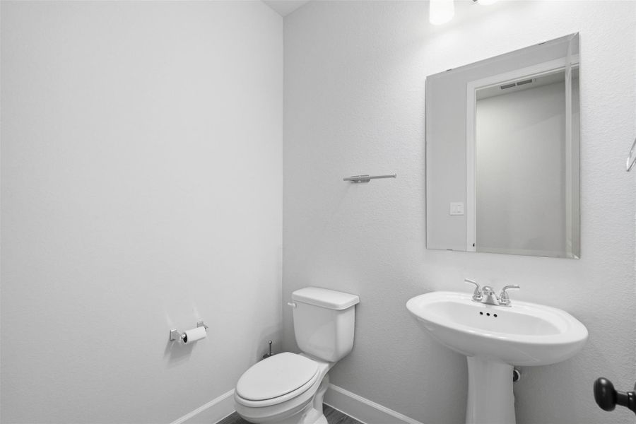 A modern, minimalist bathroom with a pedestal sink, toilet, and large mirror. The space is well-lit and has a clean, neutral design. A modern, minimalist bathroom with a pedestal sink, toilet, and large mirror. The space is well-lit and has a clean, neutral design.