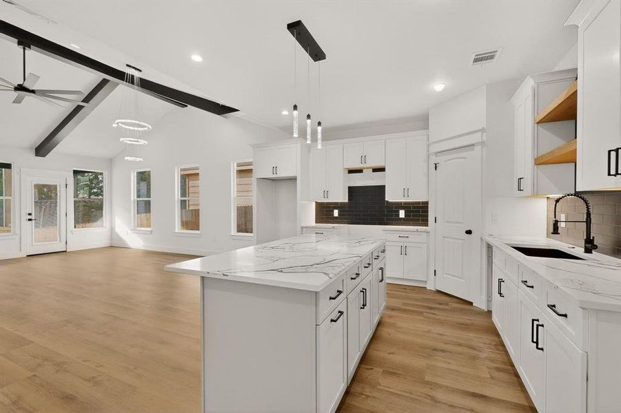 Kitchen with a center island, light stone counters, light wood-style floors, vaulted ceiling with beams, and open floor plan Kitchen with a center island, light stone counters, light wood-style floors, vaulted ceiling with beams, and open floor plan
