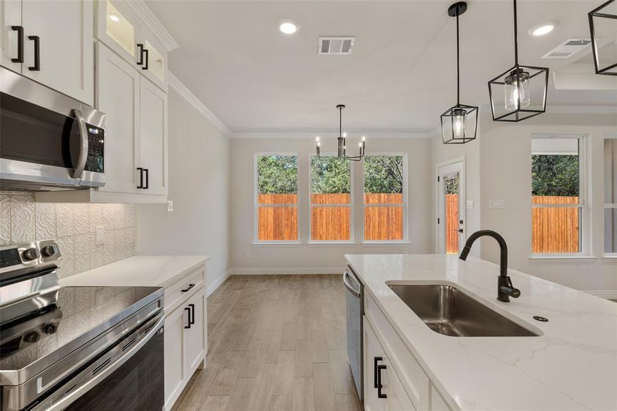 Kitchen with pendant lighting, stainless steel appliances, sink, decorative backsplash, and white cabinets