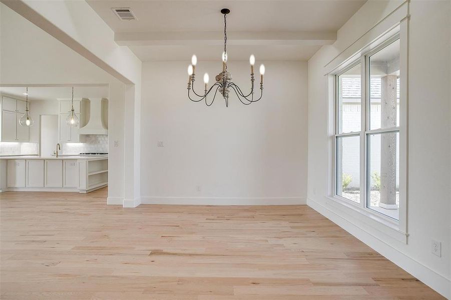 Unfurnished dining area with a chandelier, light wood-style flooring, baseboards, and beam ceiling