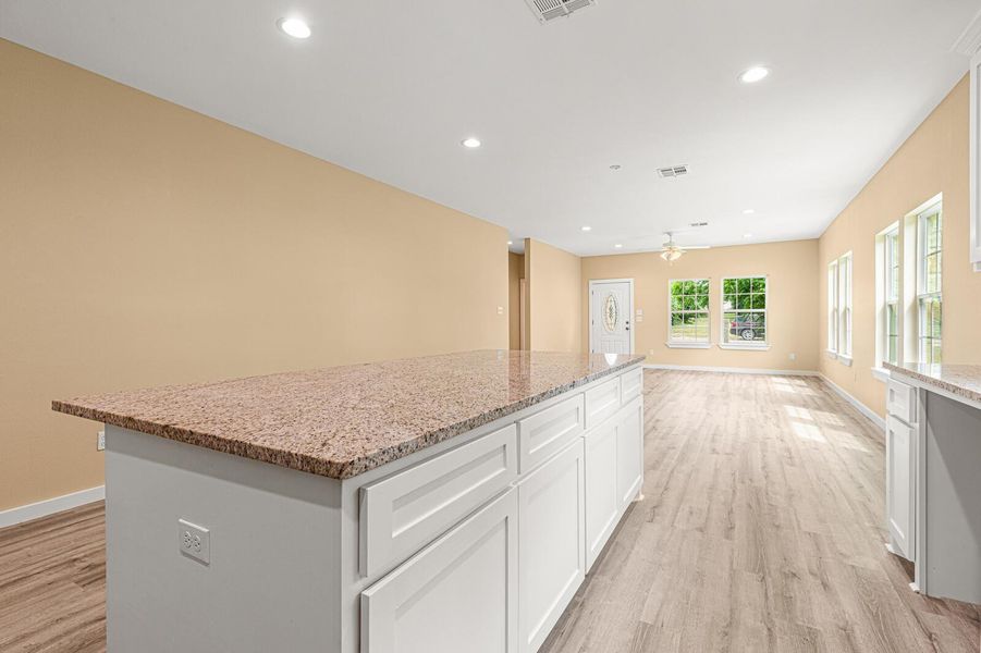 Kitchen featuring light wood finished floors, a center island, ceiling fan, light stone counters, and white cabinetry