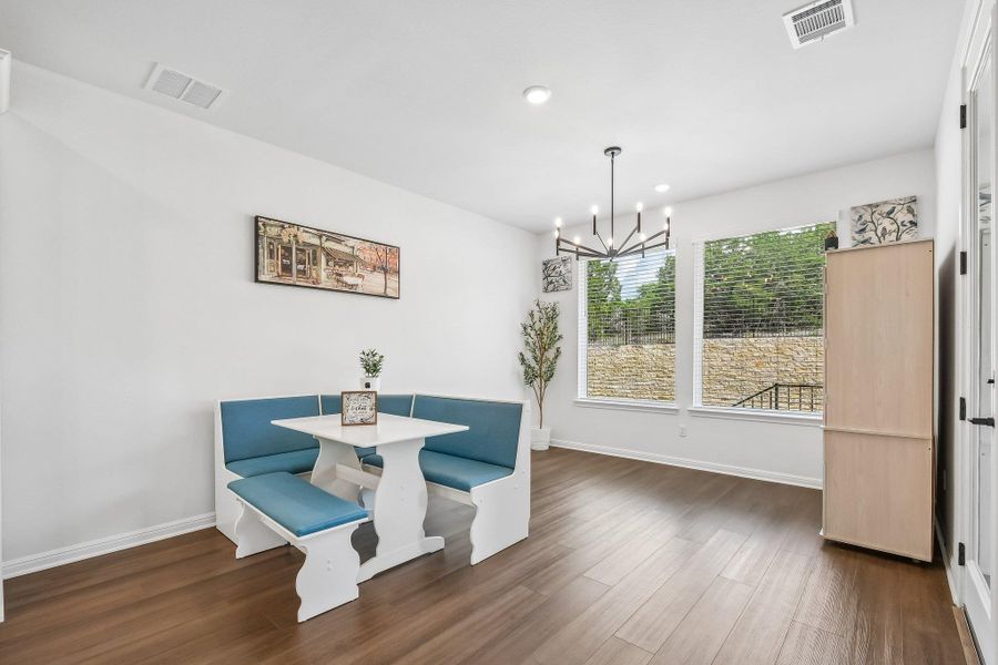 A cheerful eating area features large windows overlooking a stone wall and rich hardwood flooring.