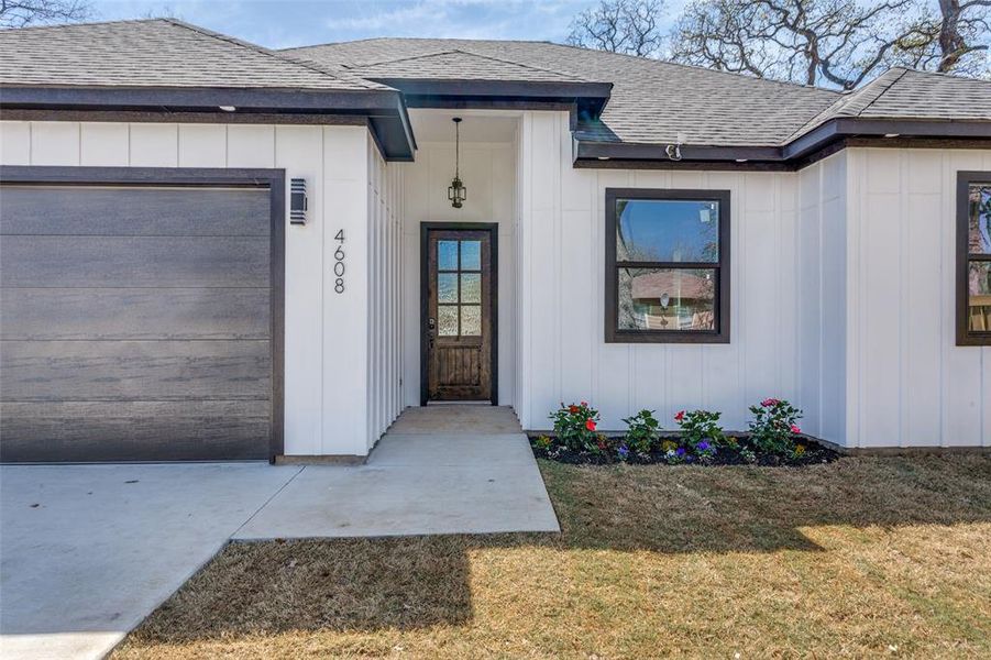 Entrance to property featuring a yard, board and batten siding, a shingled roof, and a garage