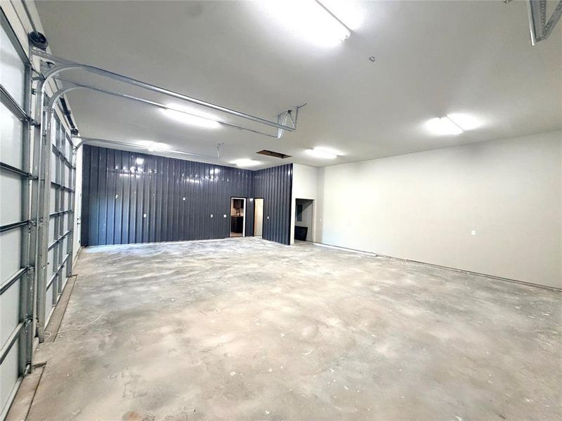 Spacious interior featuring a large roll-up door, concrete flooring, high ceilings, multiple fluorescent light fixtures, and a textured accent wall Spacious interior featuring a large roll-up door, concrete flooring, high ceilings, multiple fluorescent light fixtures, and a textured accent wall