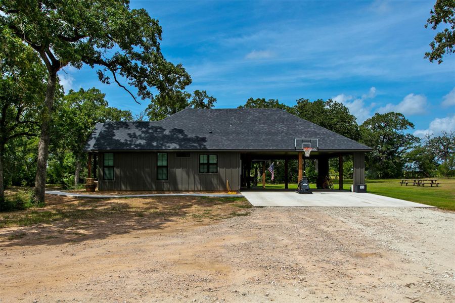 Rear view of property with driveway, an attached carport, board and batten siding, a lawn, and a shingled roof