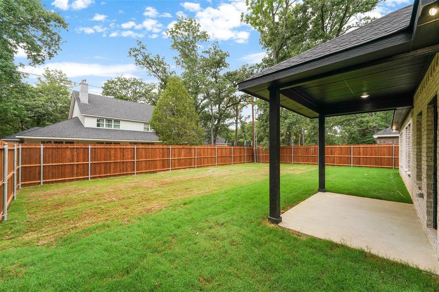 Expansive backyard featuring a new wood privacy fence, a covered patio with recessed lighting, and a brick exterior with multiple windows Expansive backyard featuring a new wood privacy fence, a covered patio with recessed lighting, and a brick exterior with multiple windows