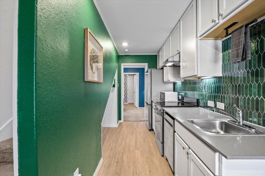 Kitchen with a textured wall, stainless steel appliances, light wood-style flooring, white cabinets, and decorative backsplash Kitchen with a textured wall, stainless steel appliances, light wood-style flooring, white cabinets, and decorative backsplash