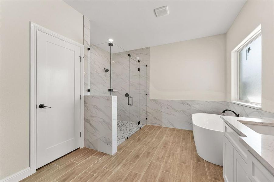 Bathroom featuring vanity, a freestanding bath, tile walls, a marble finish shower, and a wainscoted wall