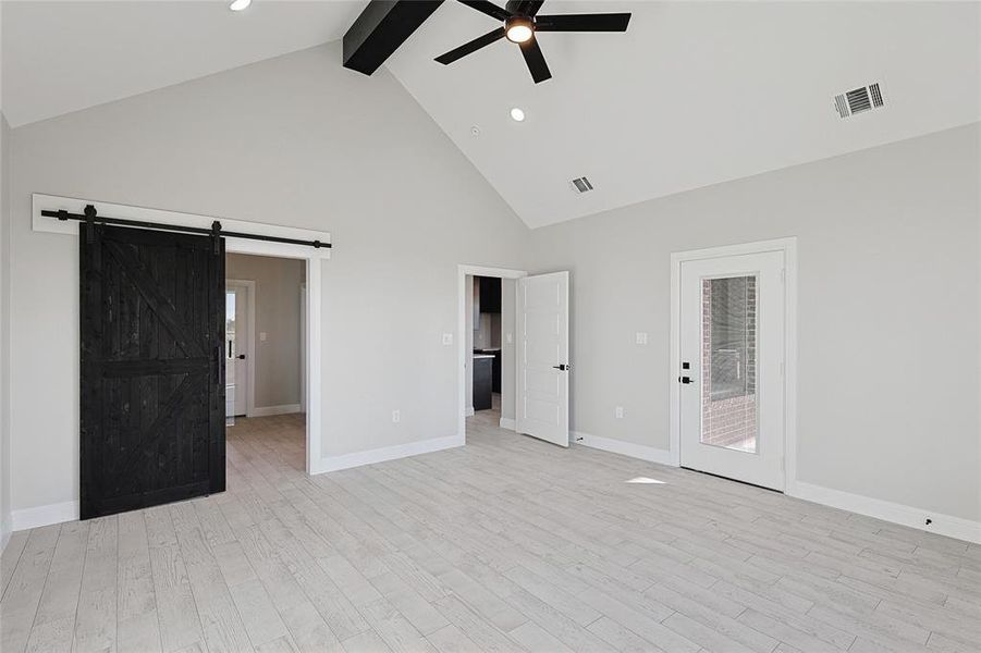 Unfurnished bedroom with ceiling fan, a barn door, light wood-type flooring, and high vaulted ceiling