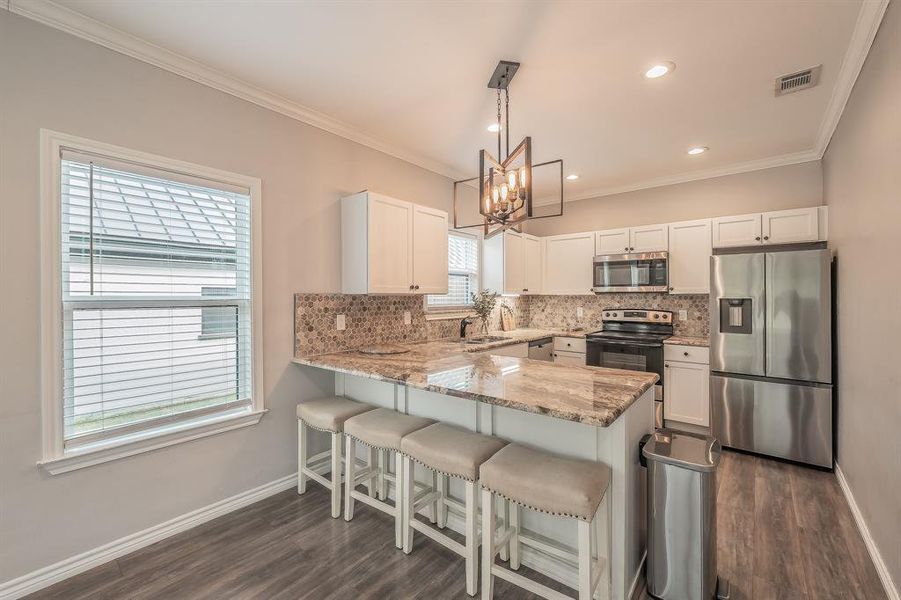 Kitchen with appliances with stainless steel finishes, tasteful backsplash, a breakfast bar area, white cabinetry, and hanging light fixtures Kitchen with appliances with stainless steel finishes, tasteful backsplash, a breakfast bar area, white cabinetry, and hanging light fixtures